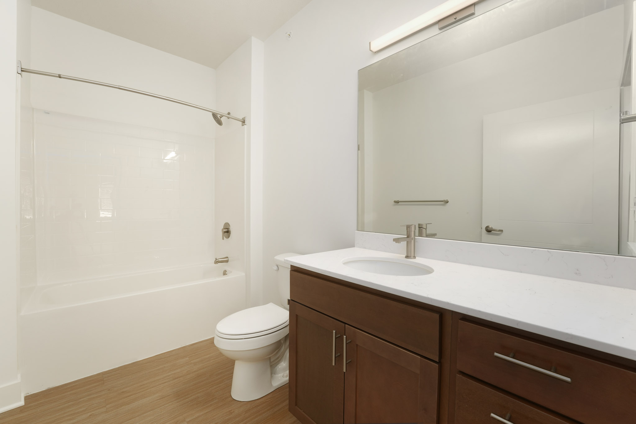 Spacious bathroom with quartz vanity, wood cabinetry, tub-shower combination, and large mirror.