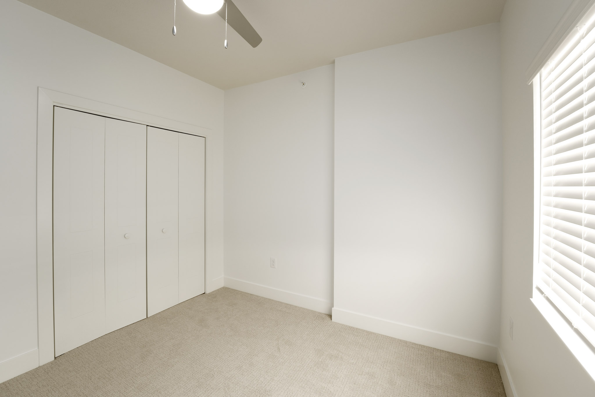 Bedroom with plush carpeting, ceiling fan, window blinds, and double-door closet.