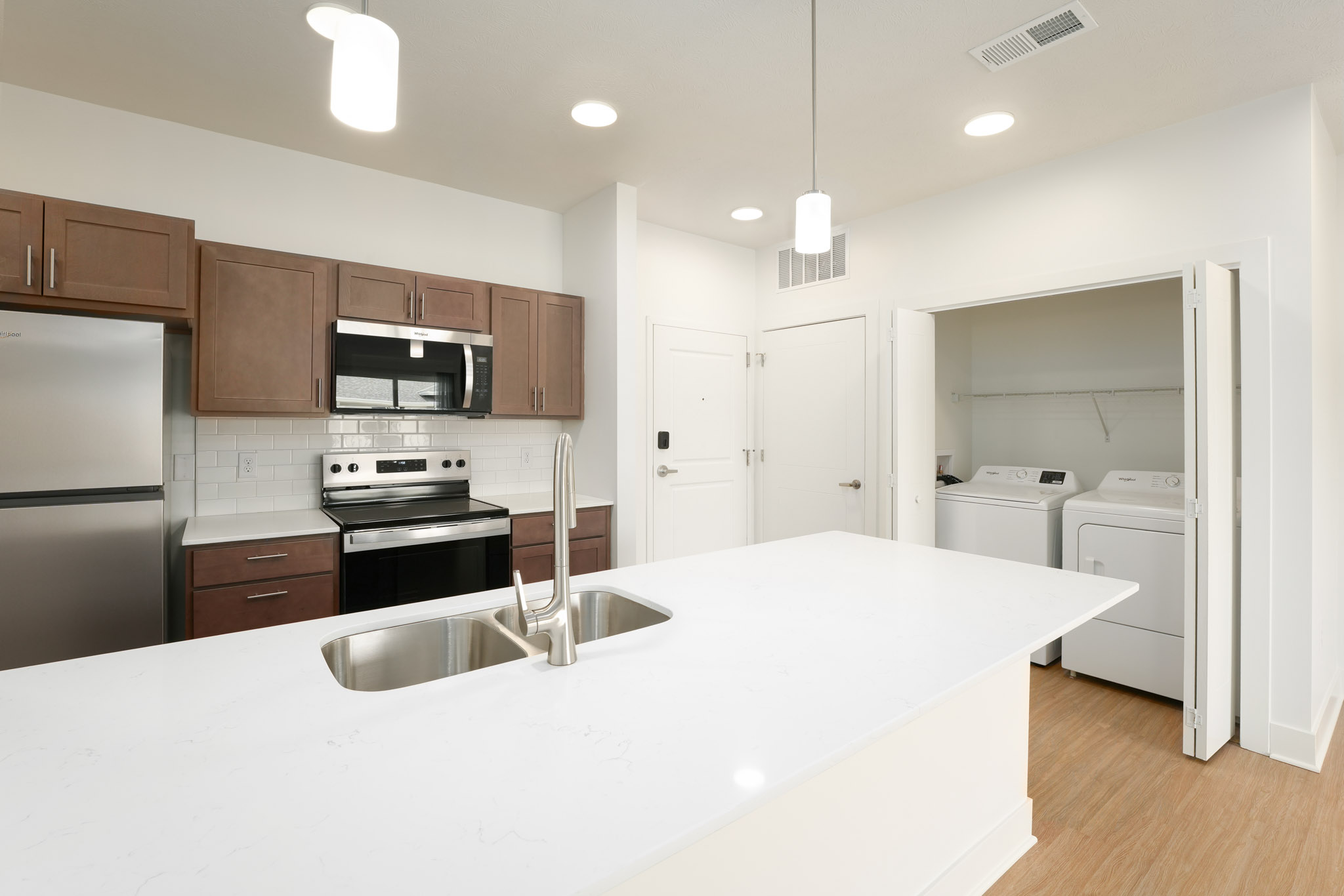 Modern kitchen with oversized island, quartz countertops, stainless steel appliances, and pantry access.