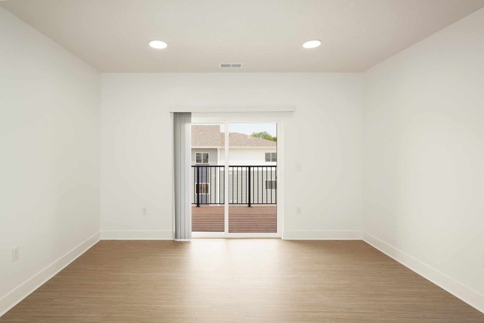 Open living room with wood-style flooring and sliding glass door to balcony.