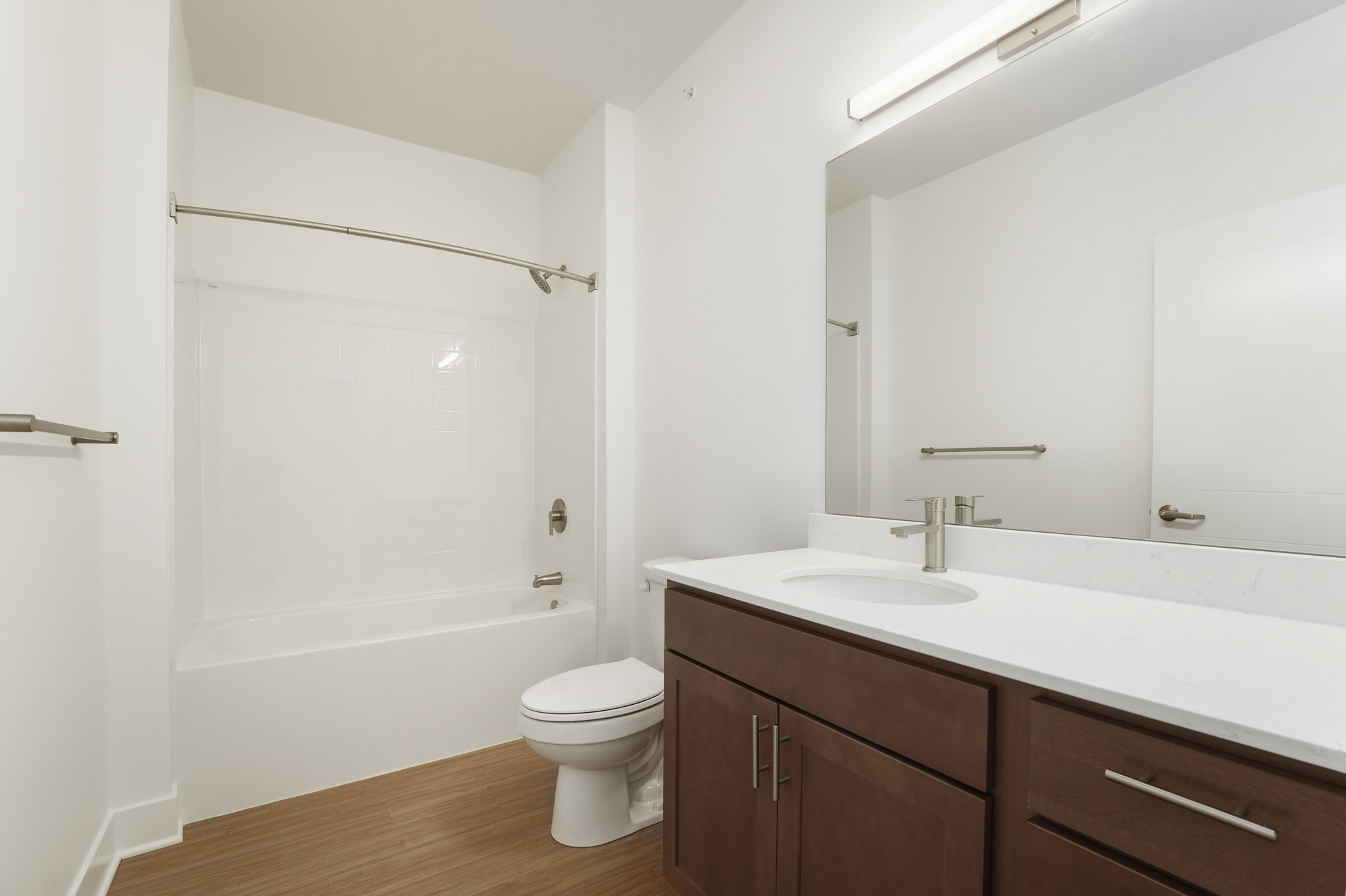 Bathroom with tub-shower combination, quartz vanity, wood cabinetry, and wood-style flooring.