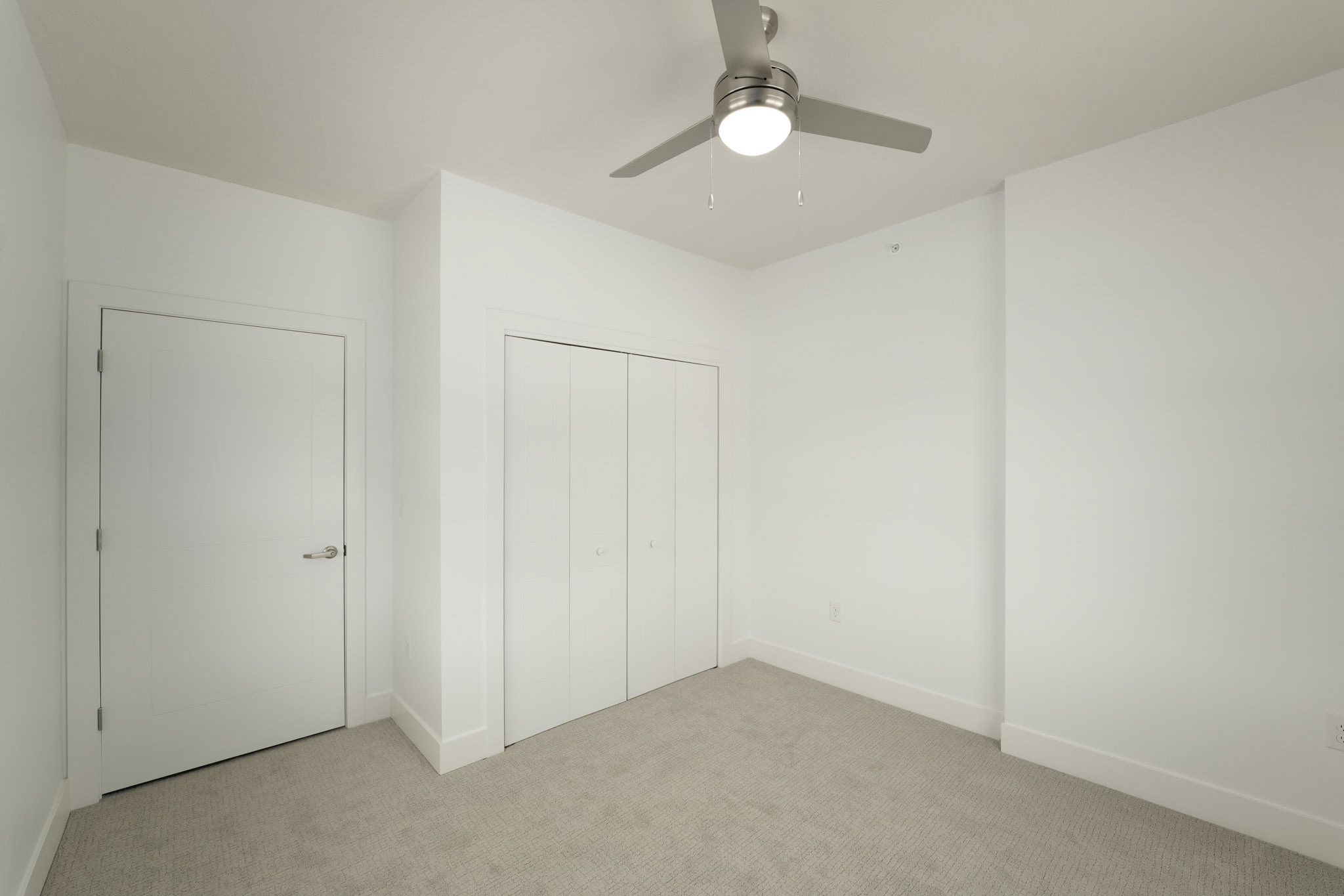 Carpeted bedroom featuring ceiling fan, double-door closet, and neutral finishes.