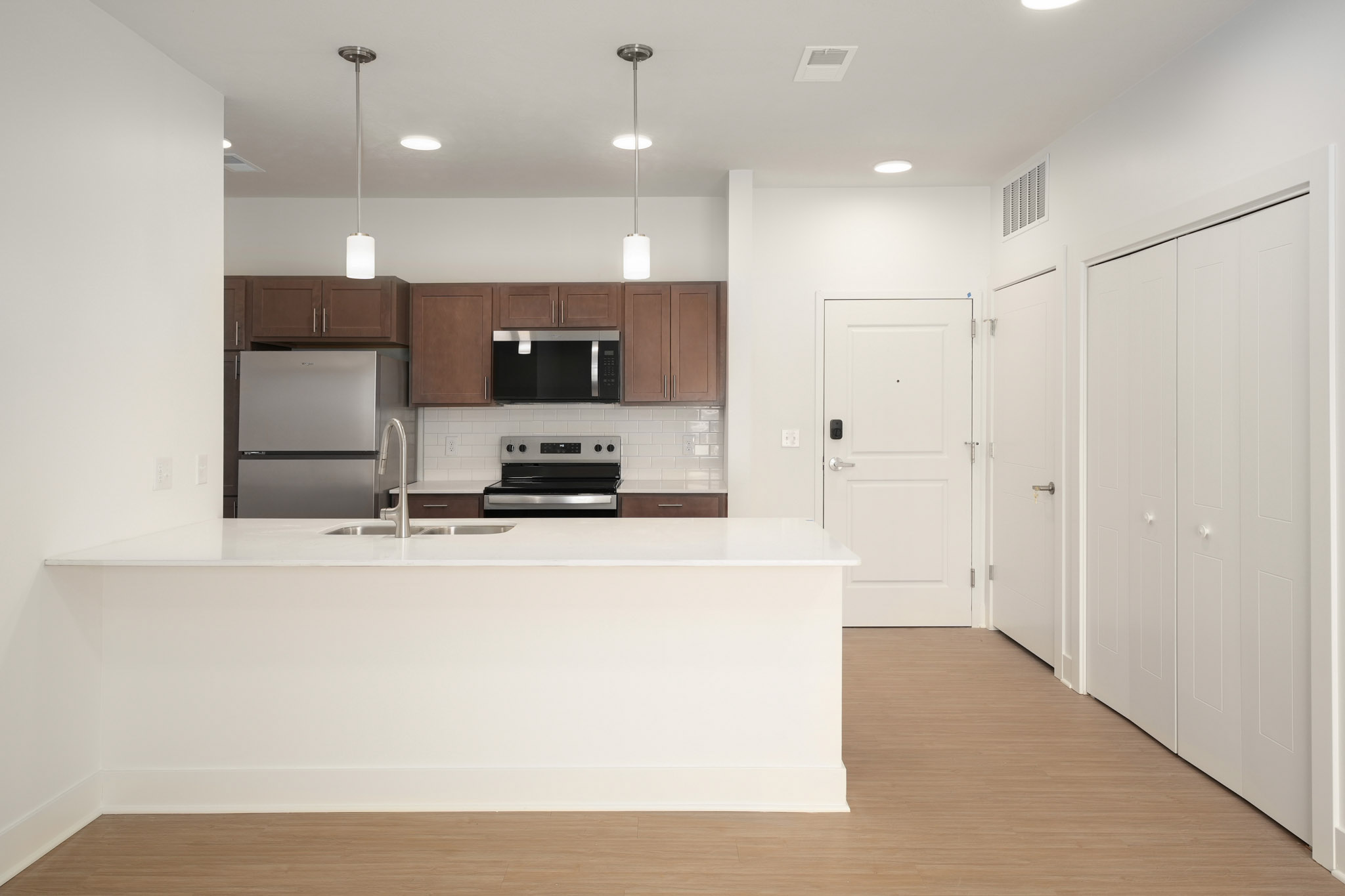 Kitchen with quartz island, stainless steel appliances, subway tile backsplash, and pendant lighting.