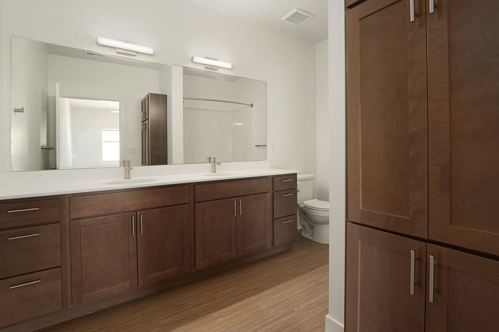 Double-sink bathroom vanity with quartz countertop, wood cabinetry, large mirror, and linen storage.