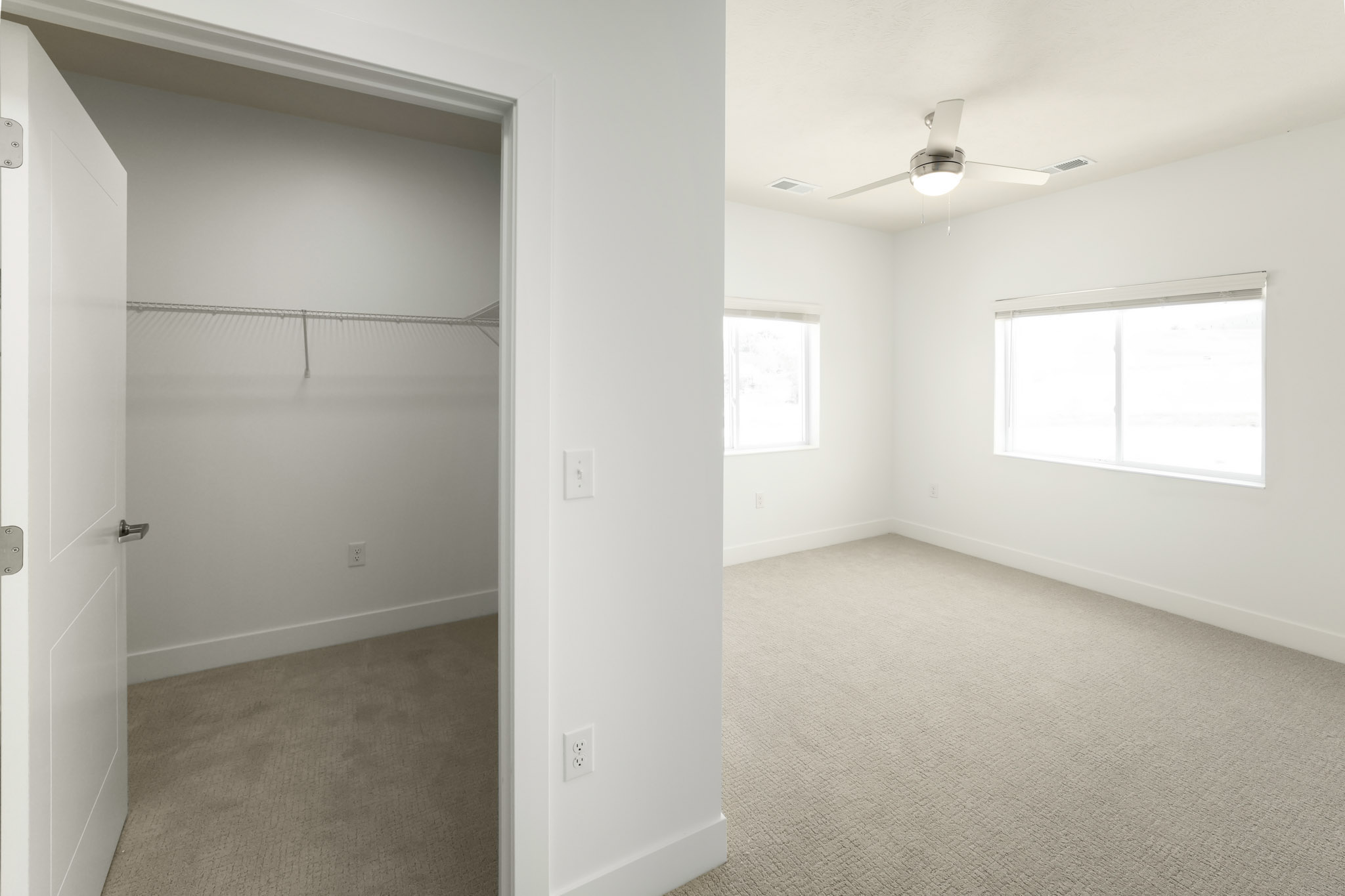 Bedroom with ceiling fan, two windows, plush carpeting, and walk-in closet.