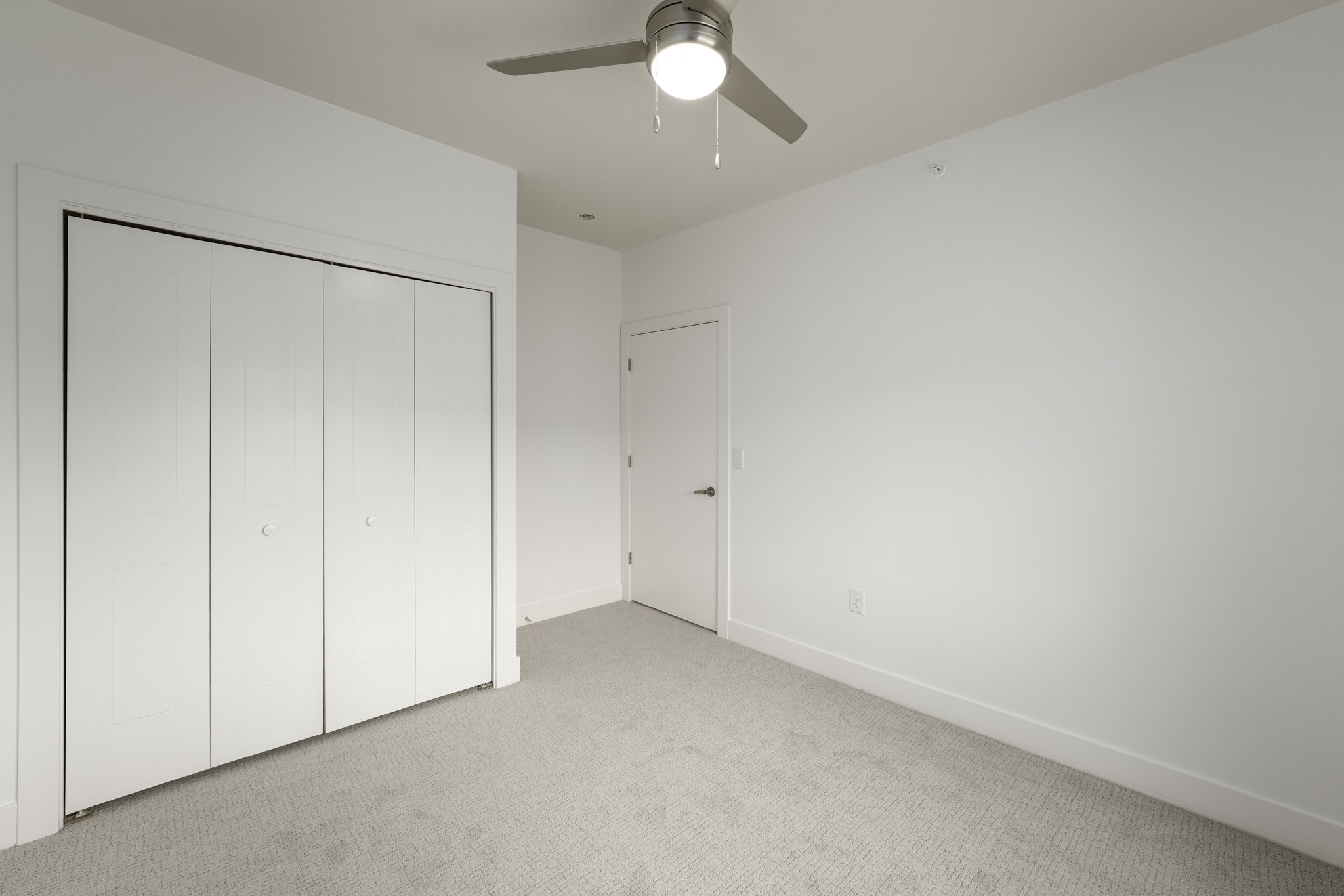 Bedroom with double-door closet, ceiling fan, plush carpeting, and white trim details.