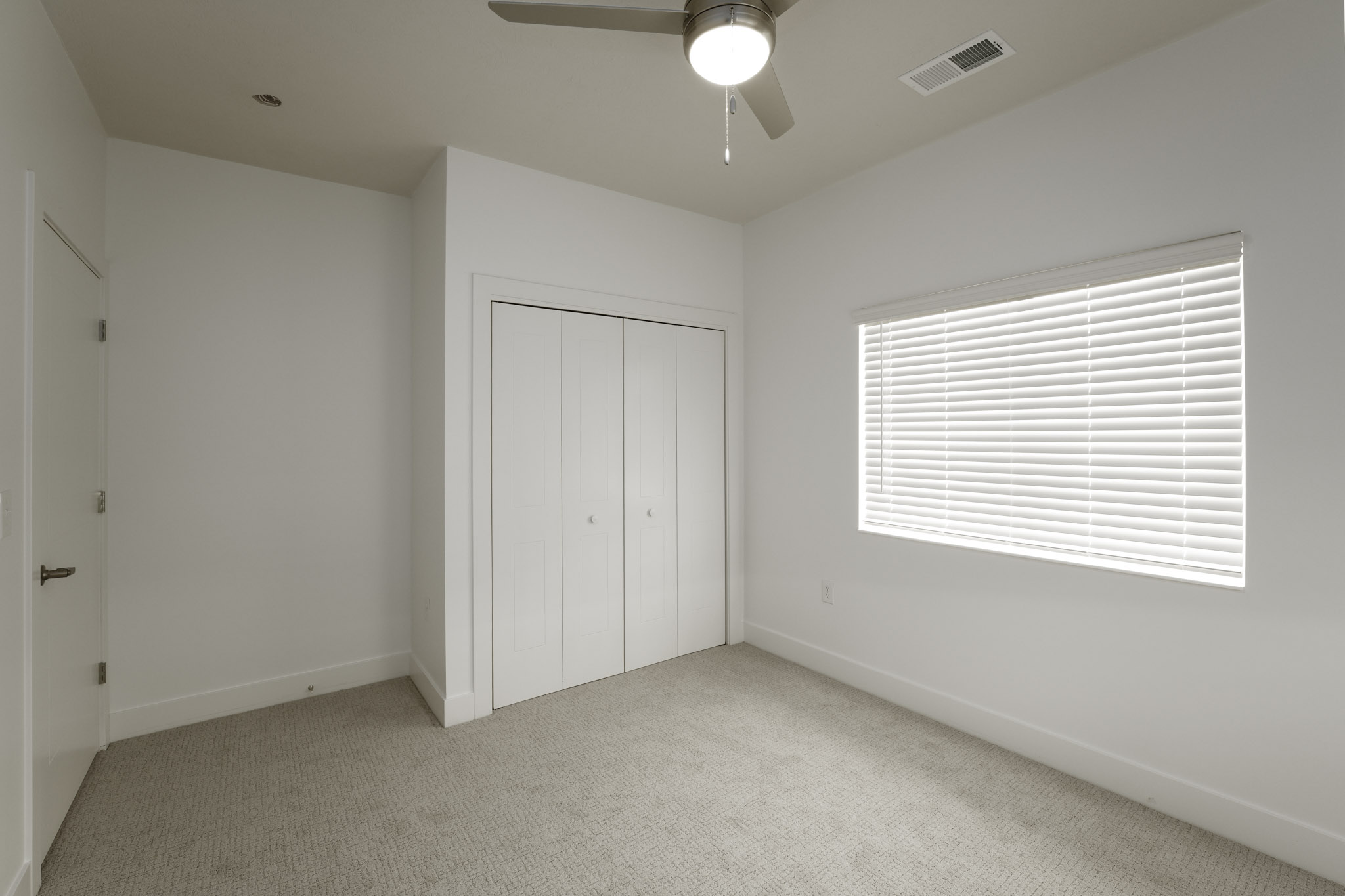 Carpeted bedroom with double-door closet, ceiling fan, and neutral finishes.
