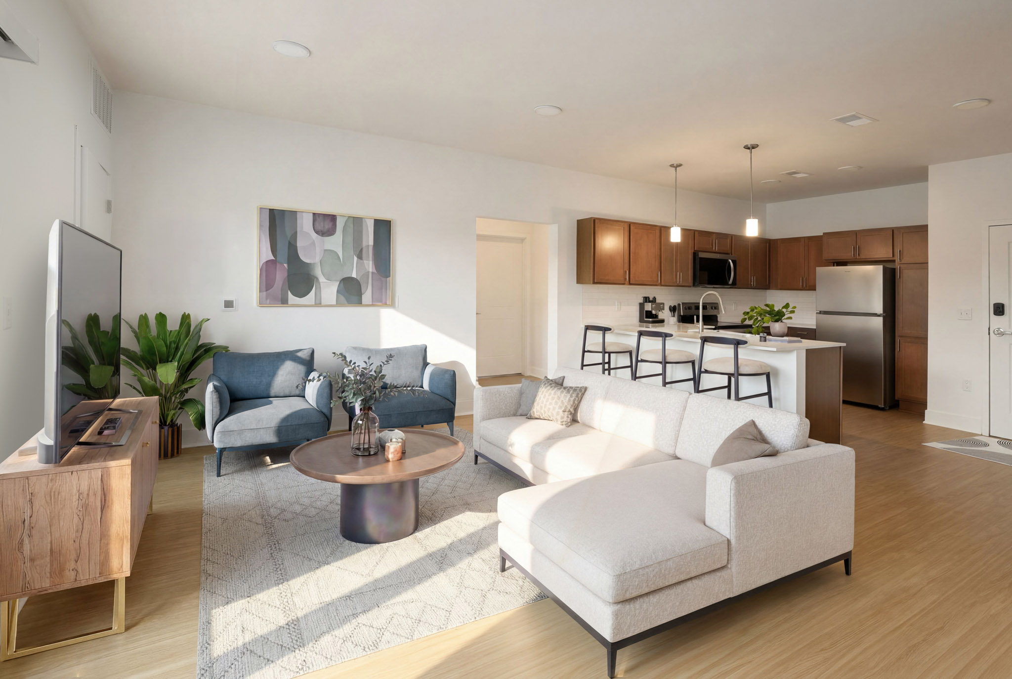 Staged living room connected to kitchen with island seating and stainless steel appliances.