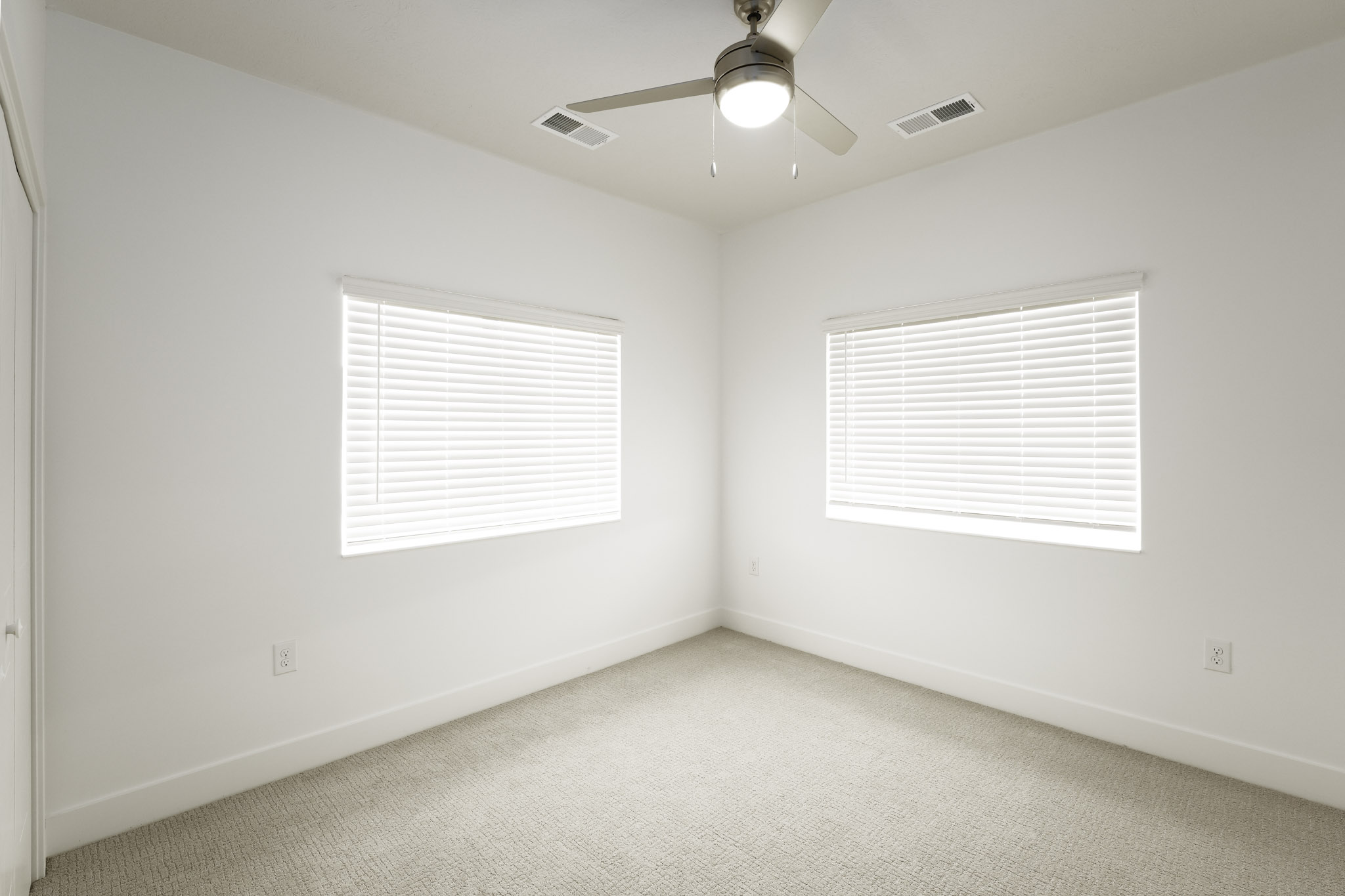 Bedroom featuring two windows, ceiling fan, plush carpeting, and bright natural light.