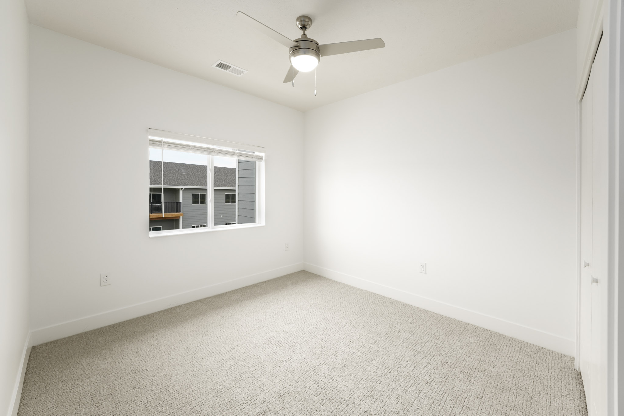 Carpeted bedroom with ceiling fan, large window, and neutral wall finishes.