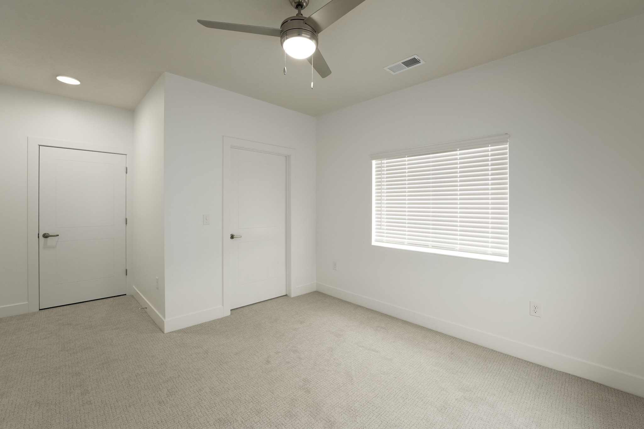 Carpeted bedroom with ceiling fan, window blinds, and neutral finishes throughout.