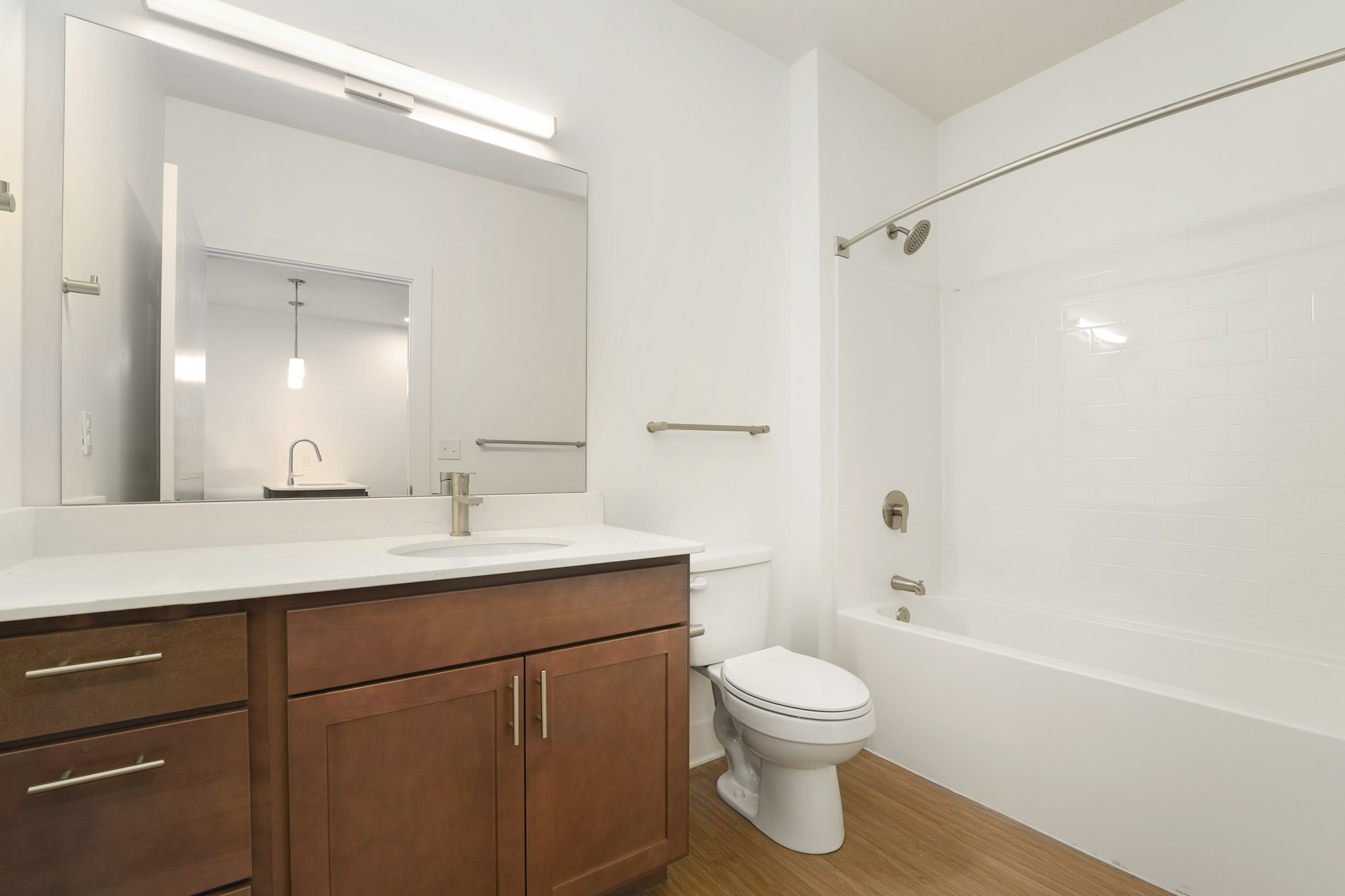 Bathroom with quartz vanity, wood cabinetry, tub-shower combination, and wood-style flooring.