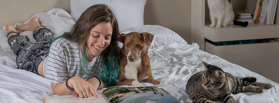 Teenager reading on the bed while with her pet dog and cat