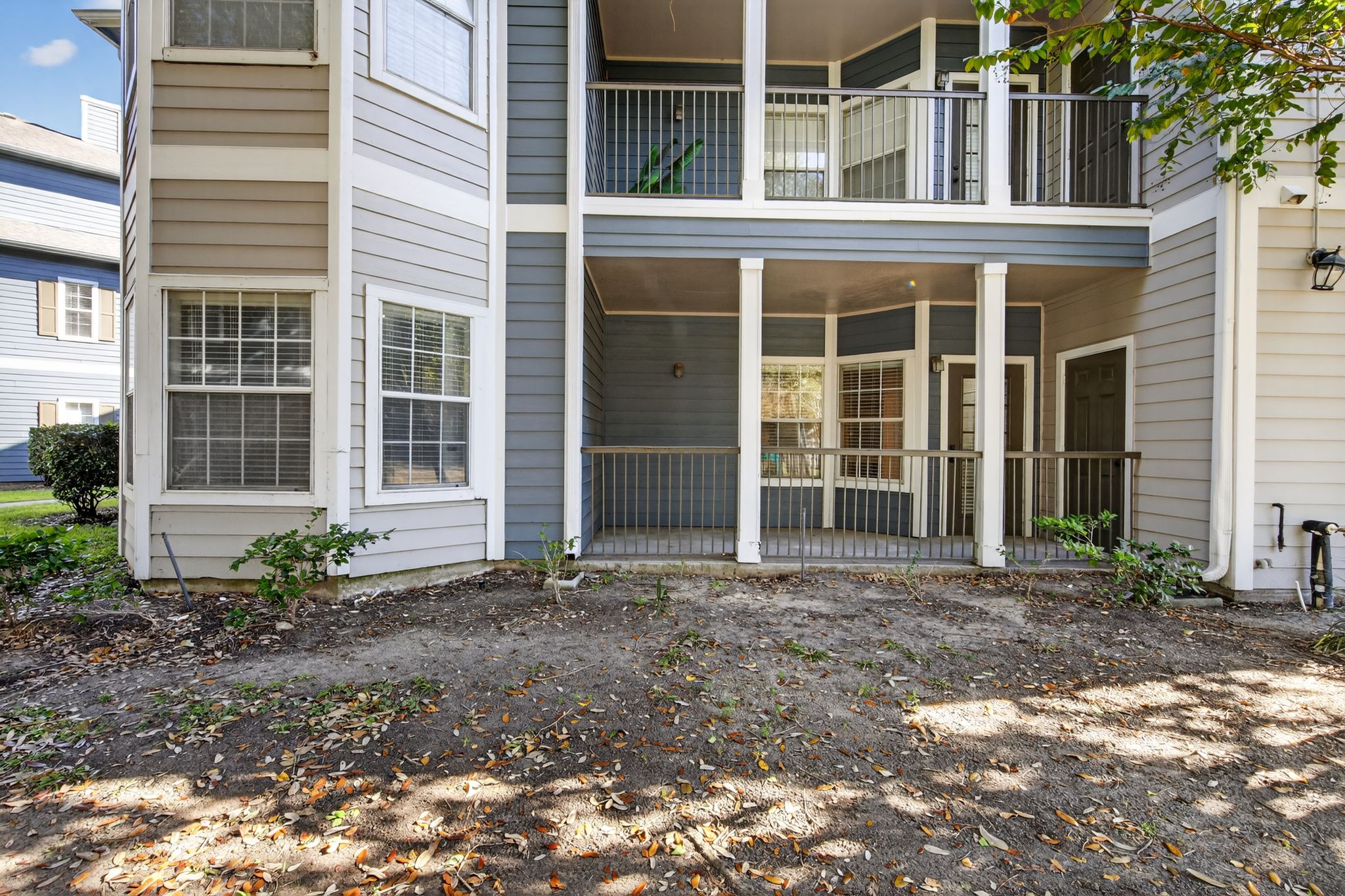 Exterior view of ground level patios with blue and beige siding, railing accents, and surrounding landscaping