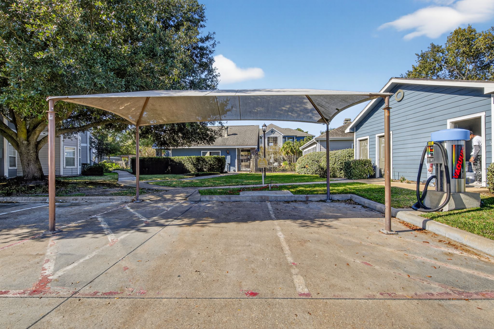 Covered car wash station with shade canopy, vacuum equipment, marked parking bays, and landscaped paths throughout the community