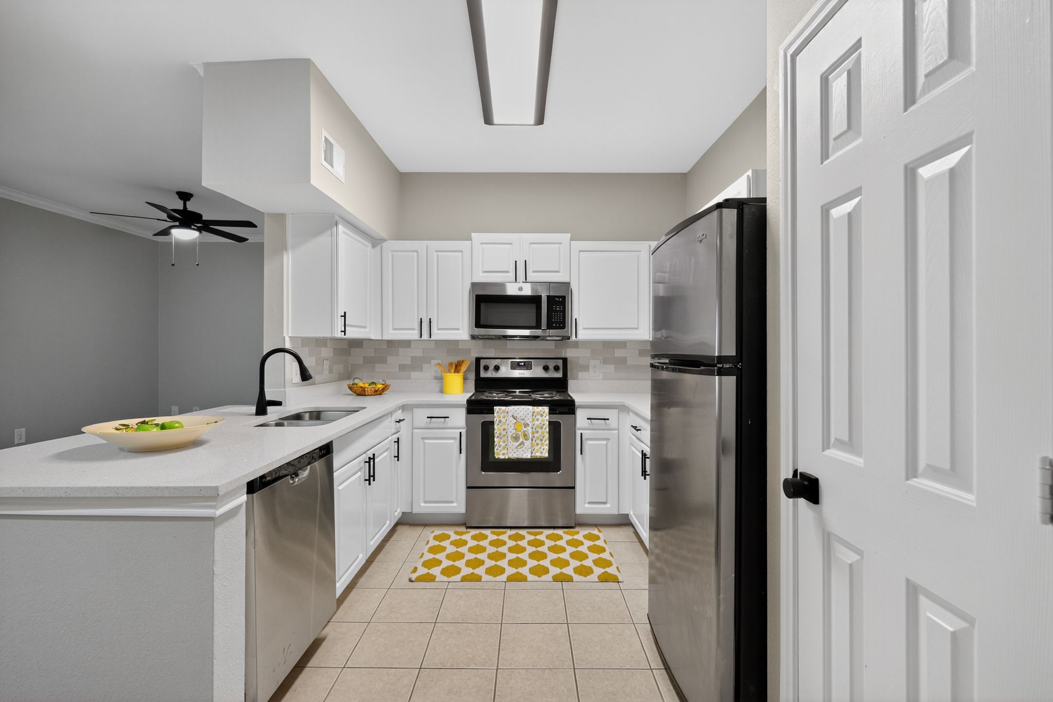 Kitchen with white cabinets, stainless steel appliances, bright lighting, and a patterned yellow rug by the stove