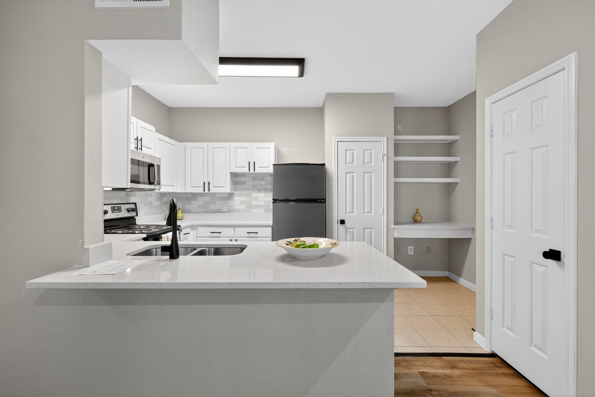 Bright kitchen with white cabinetry, quartz counters, stainless appliances, and a built in desk area with open shelving