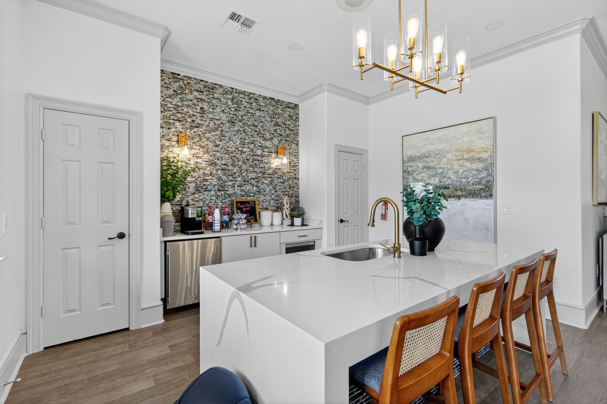 Resident clubhouse kitchen with quartz island, bar seating, modern lighting, stainless appliances, and mosaic tile backsplash