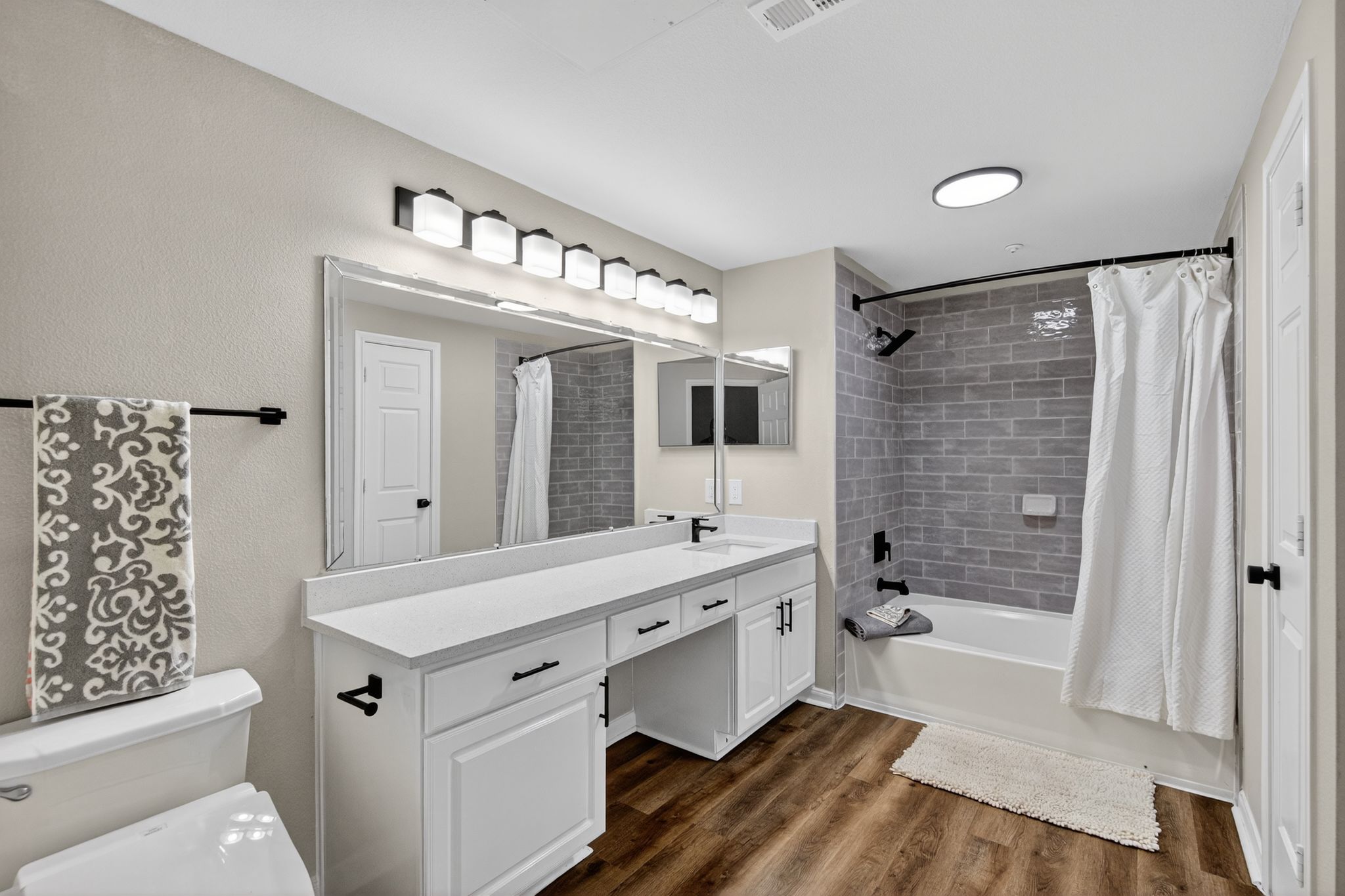 Spacious bathroom with long vanity, large framed mirror, gray tiled shower wall, and modern black fixtures