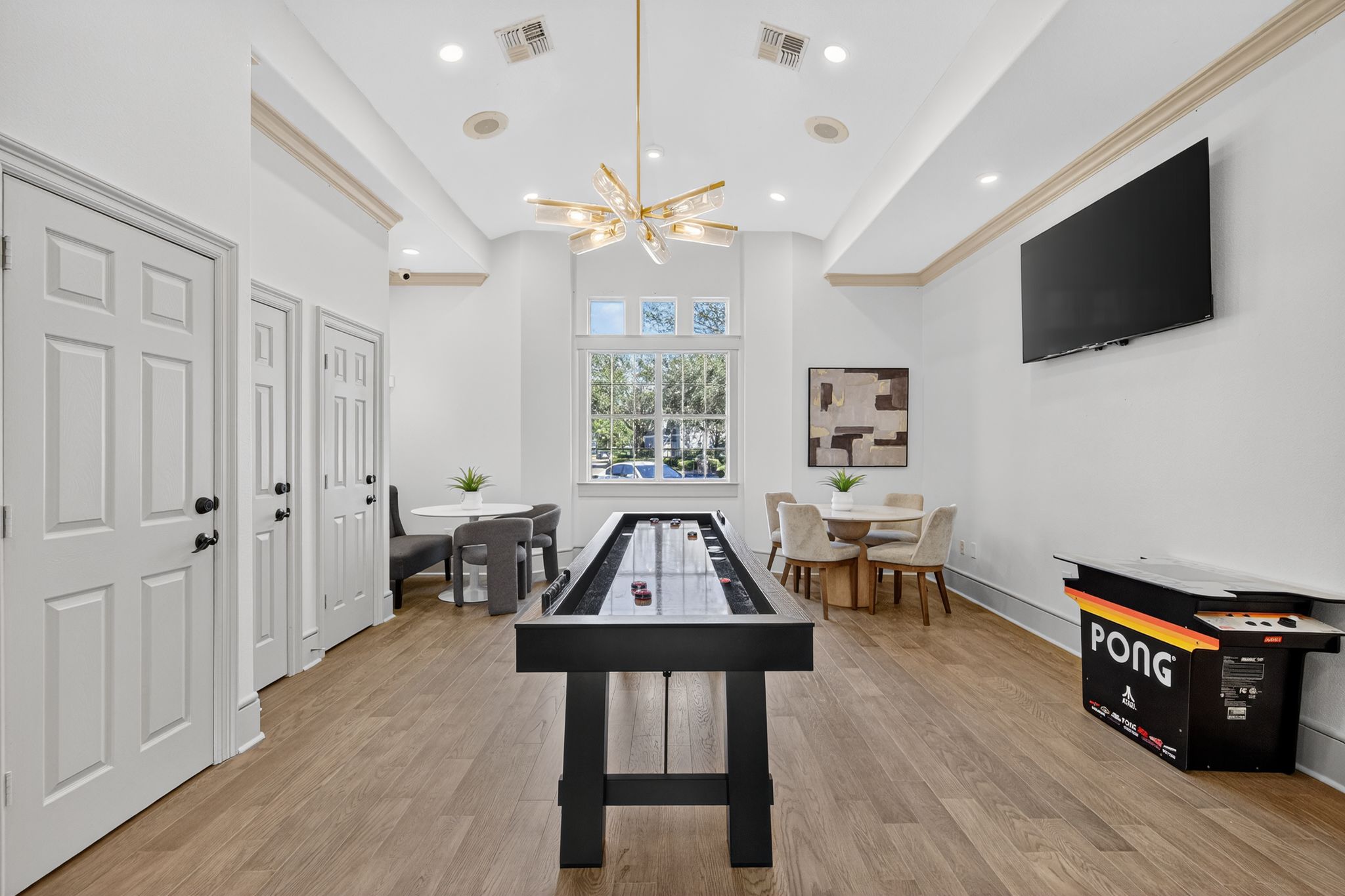 Community game room featuring a shuffleboard table, lounge seating, wall-mounted TV, and modern lighting with wood-style flooring