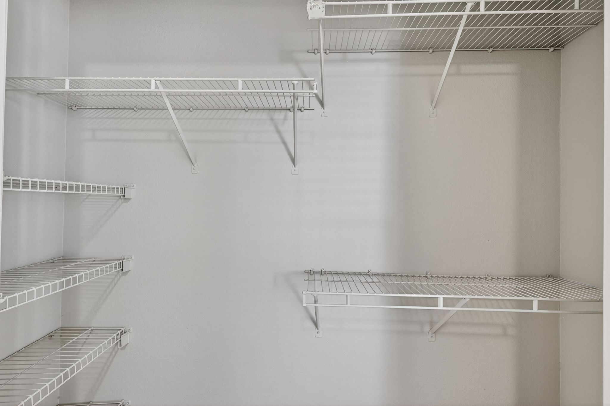 Walk in closet with multiple white wire shelves mounted on light gray walls for storage organization