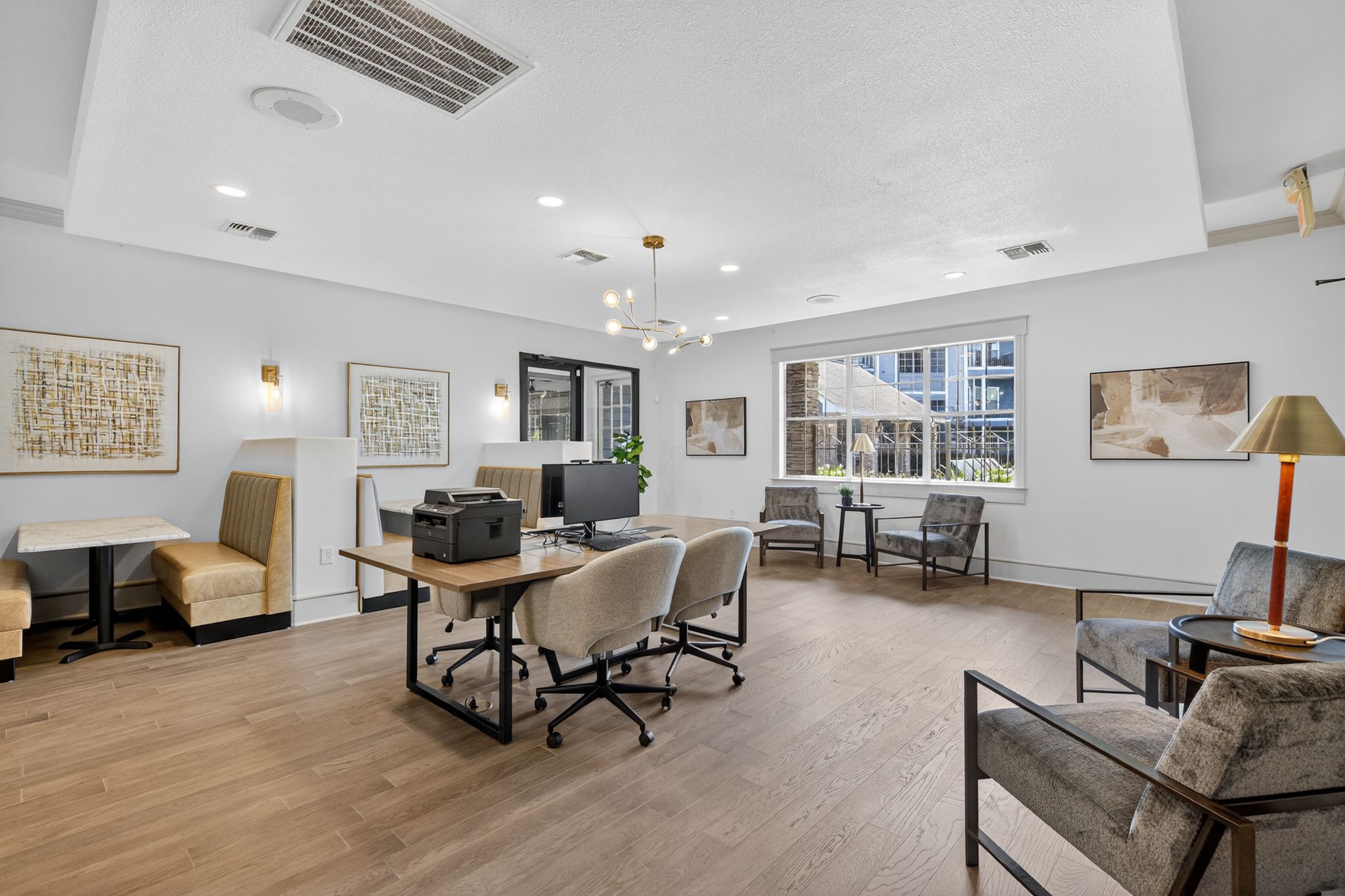 Modern resident business center with shared work tables, private booths, comfortable seating, and large windows providing natural light