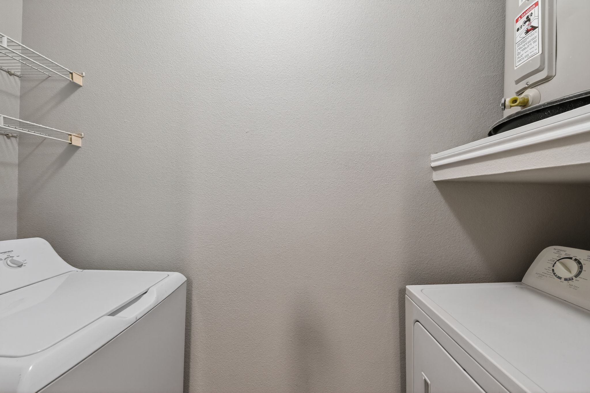 Laundry room with washer and dryer units, wall shelving on the side, and a water heater placed on an elevated shelf