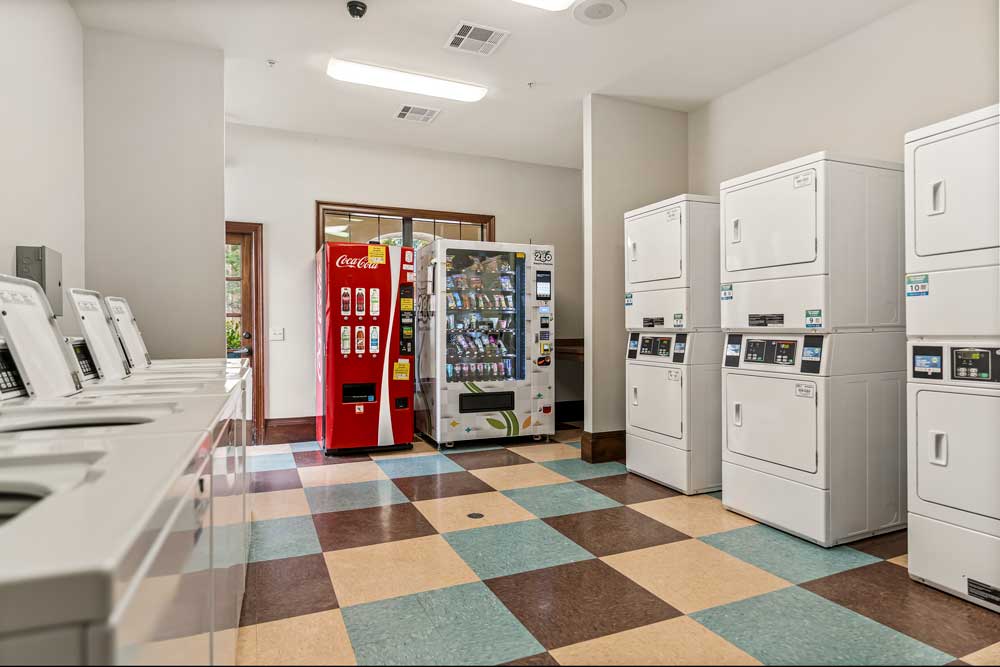 Laundry facility with washers, stacked dryers, vending machines, tiled flooring, and convenient access to outdoor entry door