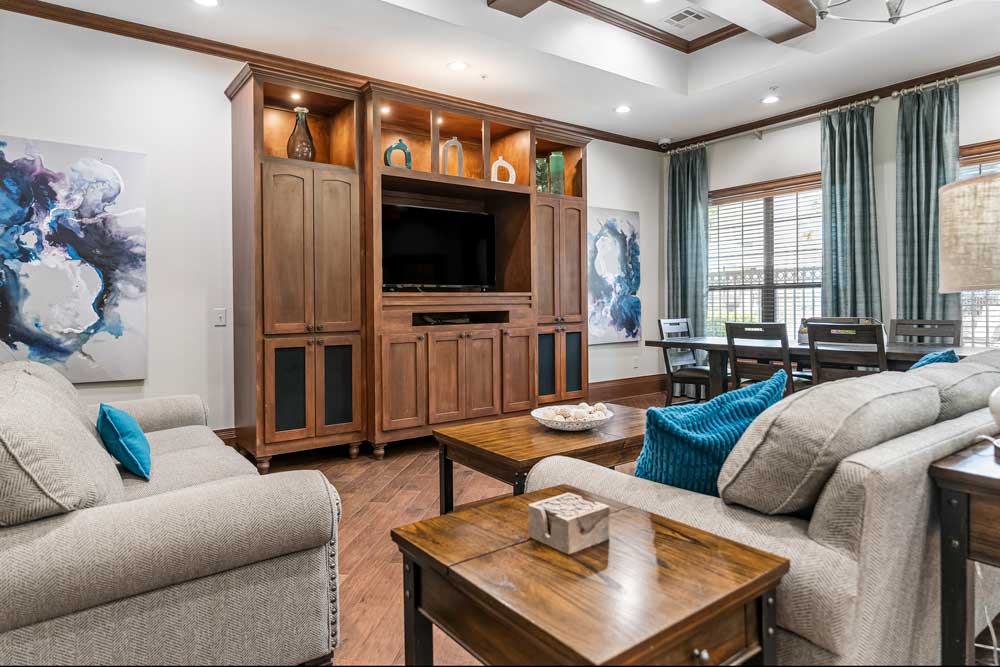 Comfortable resident lounge with sofas, wood coffee tables, built-in entertainment center, and large windows with natural light