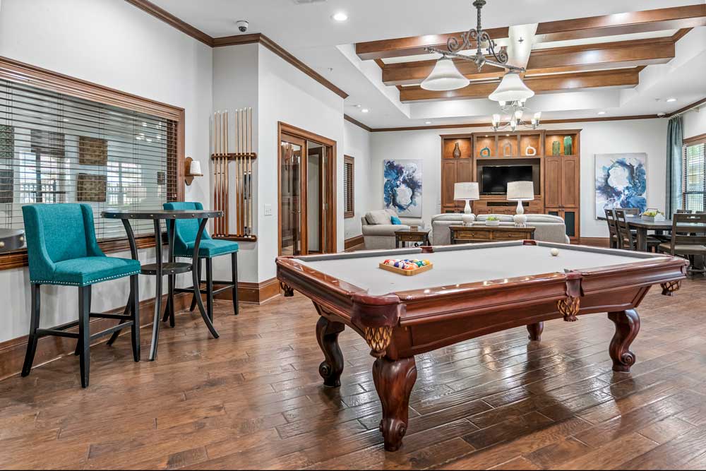 Resident game room with pool table, high-top seating, lounge area, and entertainment center with mounted television and shelving