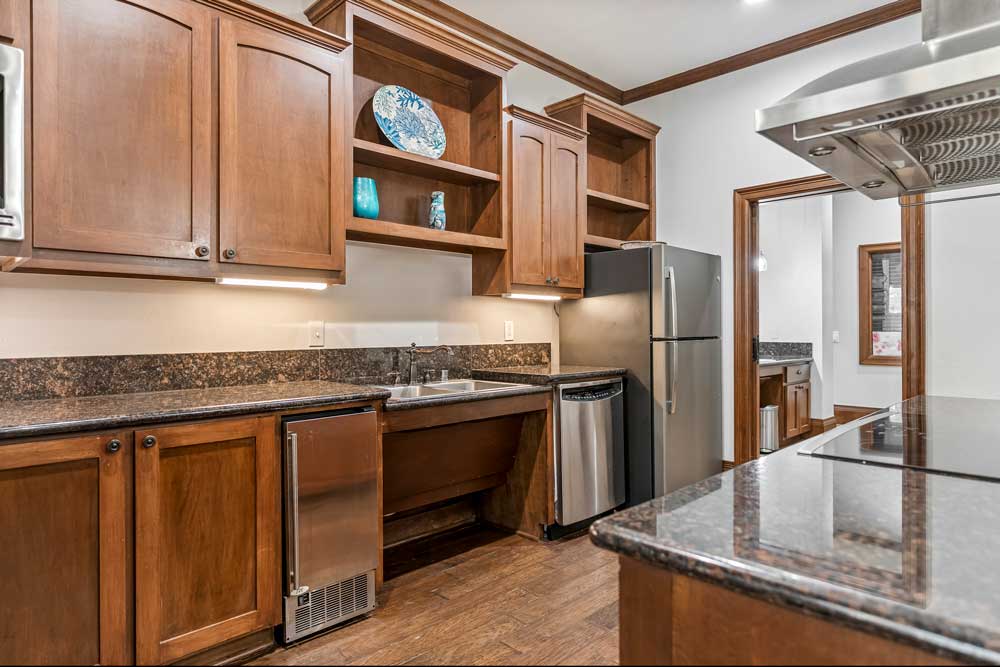 Community kitchen with wood cabinetry, granite countertops, stainless steel appliances, and open shelving for storage display