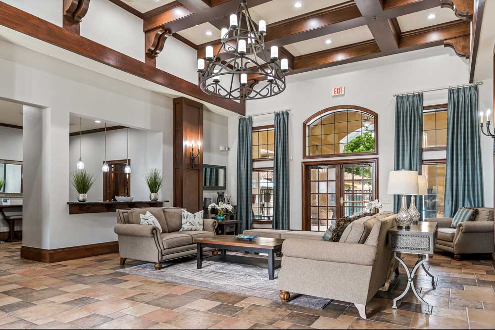 Open clubhouse interior with seating areas, coffered ceilings, chandelier, tiled flooring, and access to adjacent common spaces