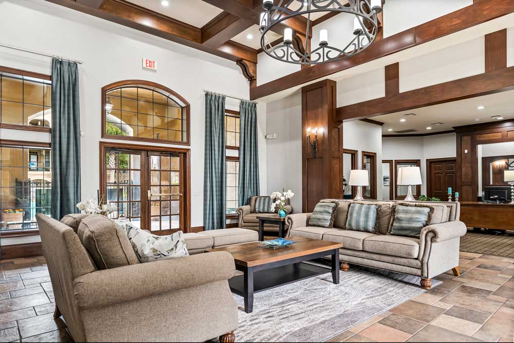 Spacious clubhouse living area with high ceilings, chandelier lighting, plush seating, and large windows bringing in natural light