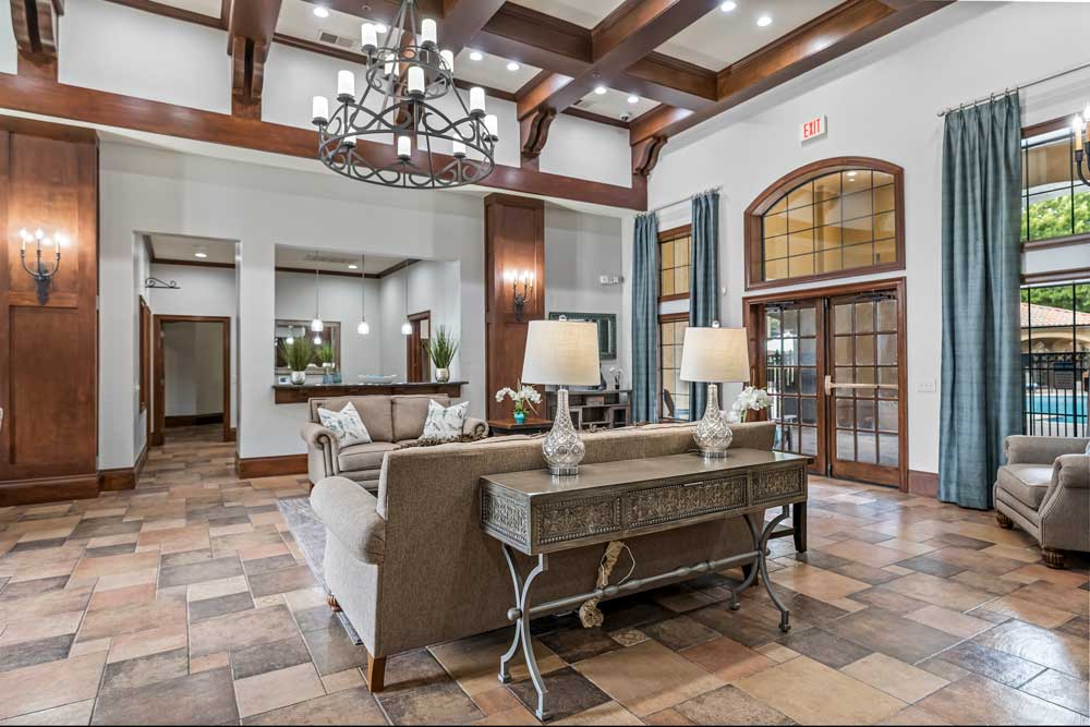 Community clubhouse interior with high ceilings, chandelier lighting, seating areas, and large windows overlooking pool area