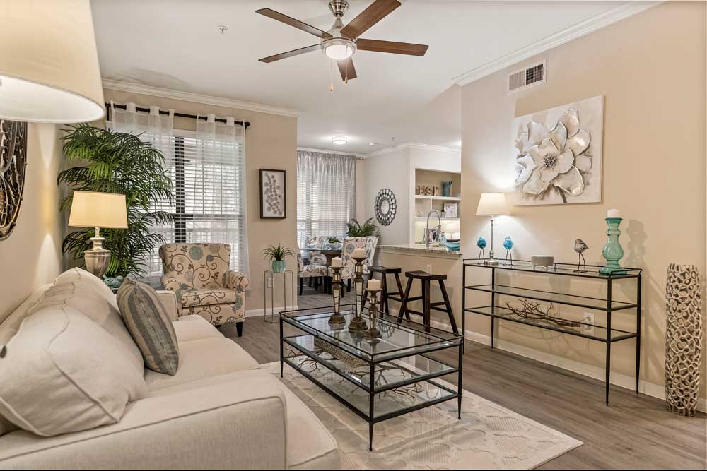 Bright living room with a beige sofa, glass coffee table, hardwood floors, and an open view to the dining area