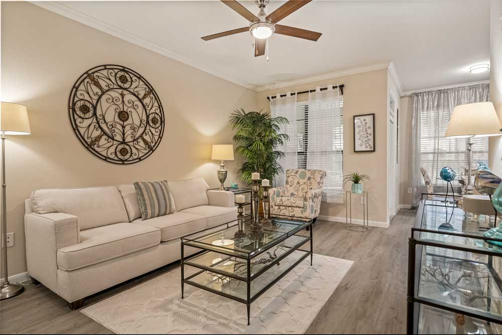 Cozy living room featuring a beige sofa, glass coffee table, decorative wall medallion, and hardwood floors with natural light