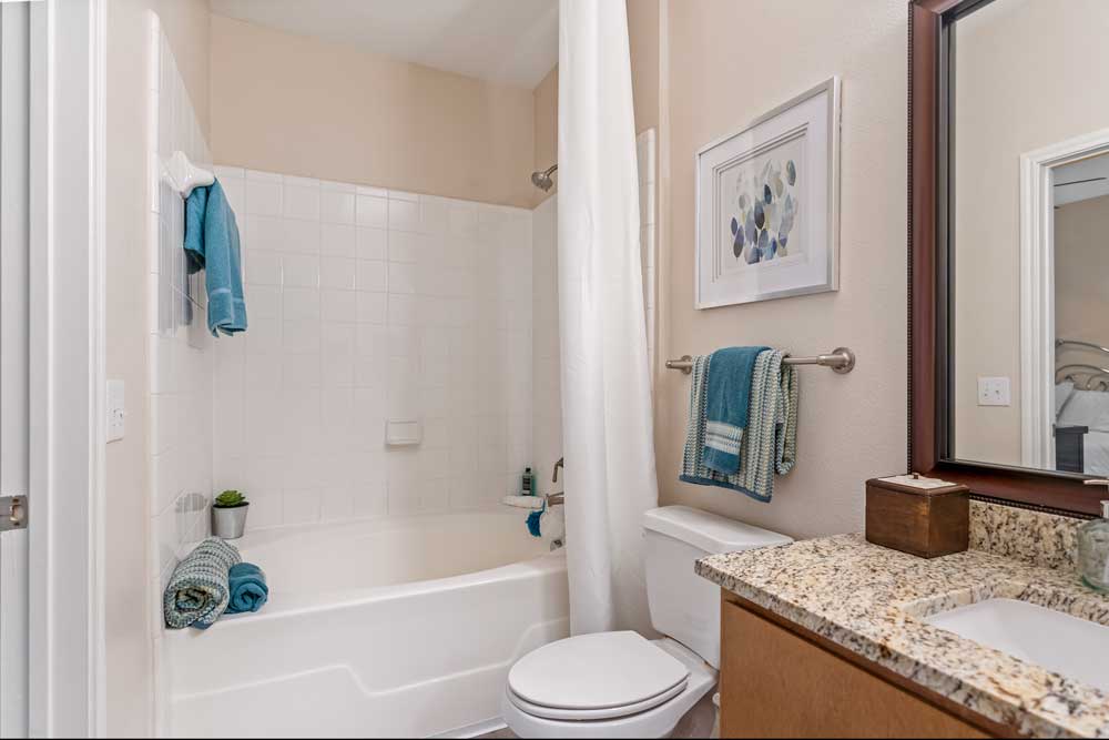 Bathroom interior featuring granite countertop, under-mount sink, bathtub with tile surround, and folded towels on rack