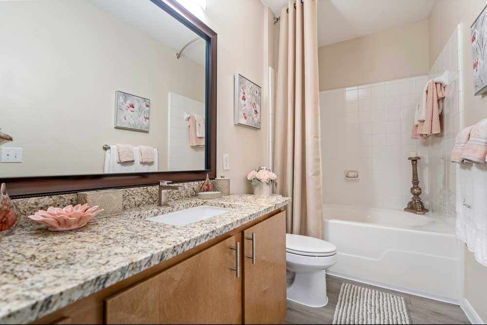 Bathroom with granite countertop, under-mount sink, framed mirror, bathtub with shower curtain, and neatly arranged towels