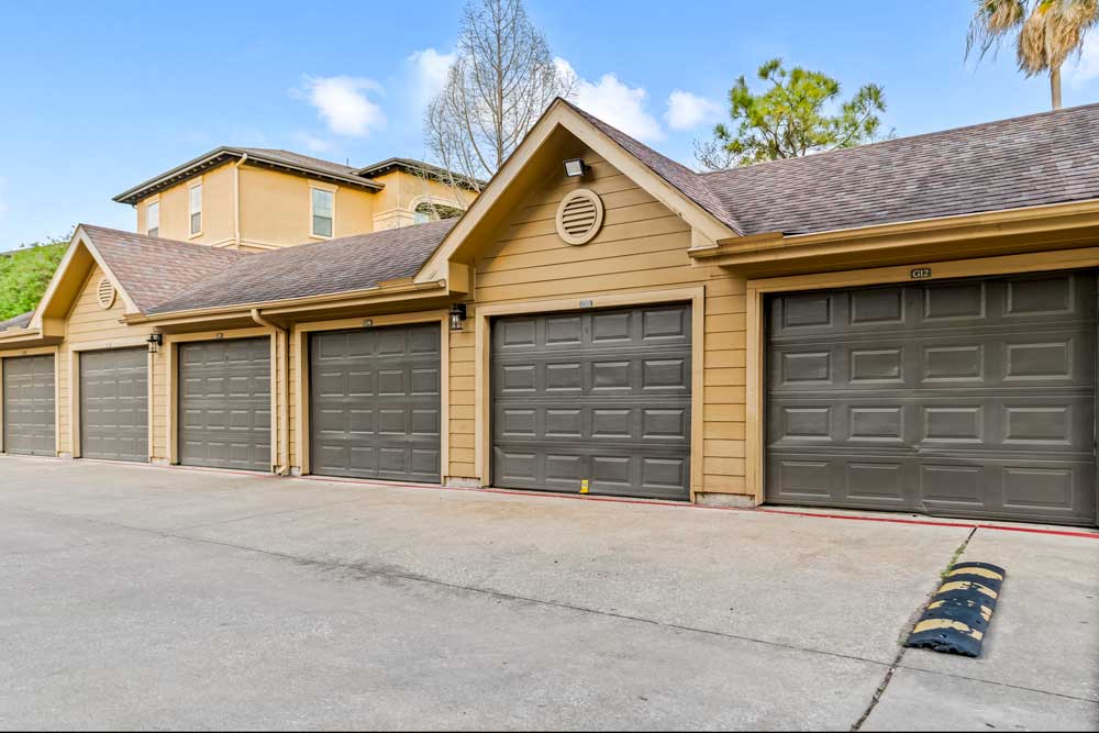 Garage buildings with multiple bays, neutral siding, and paved drive with speed bump and landscaped surroundings