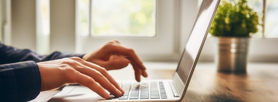 A pictured hand typing on a laptop