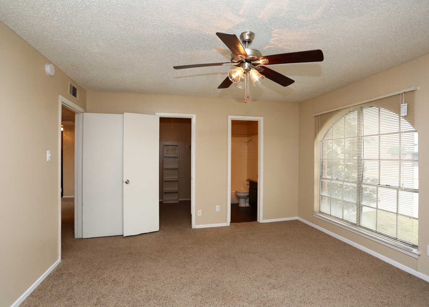 Well-Lit Bedroom with Ceiling Fan and Window Coverings at The Junction Apartments