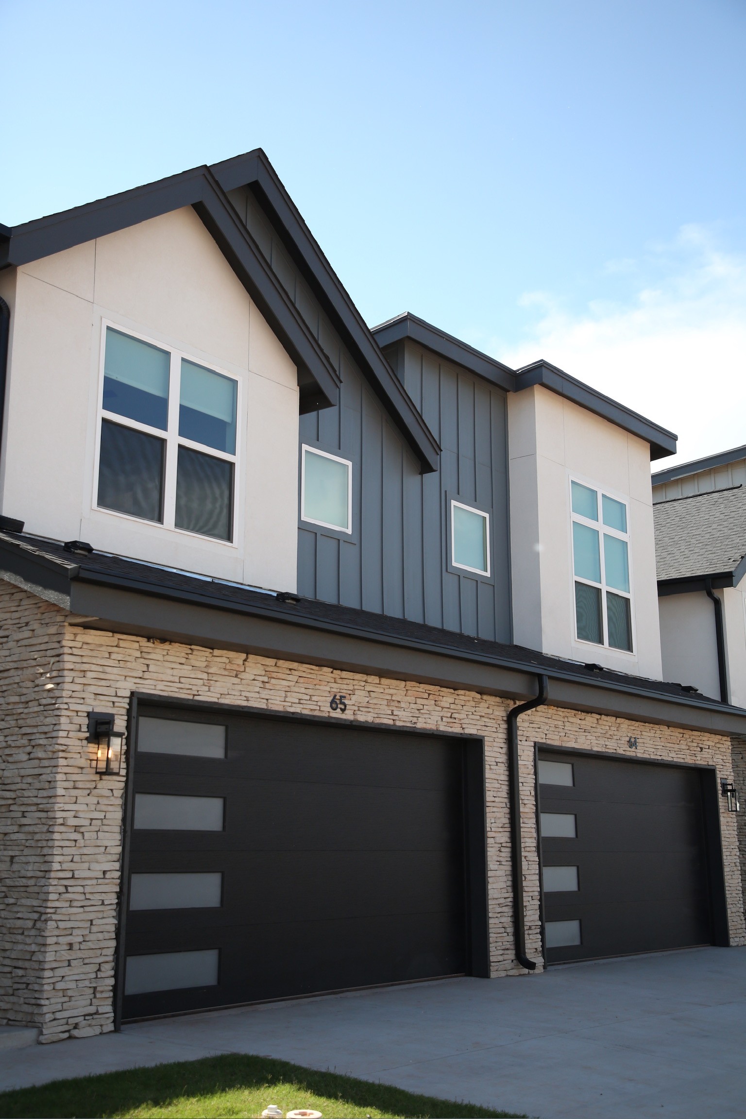 Modern townhome exteriors with stone accents, dark garage doors, board and batten siding, and private driveways at Oaks at Covell