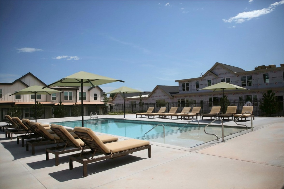  Resort-style community pool with lounge chairs, shade umbrellas, iron fencing, and townhomes in the background
