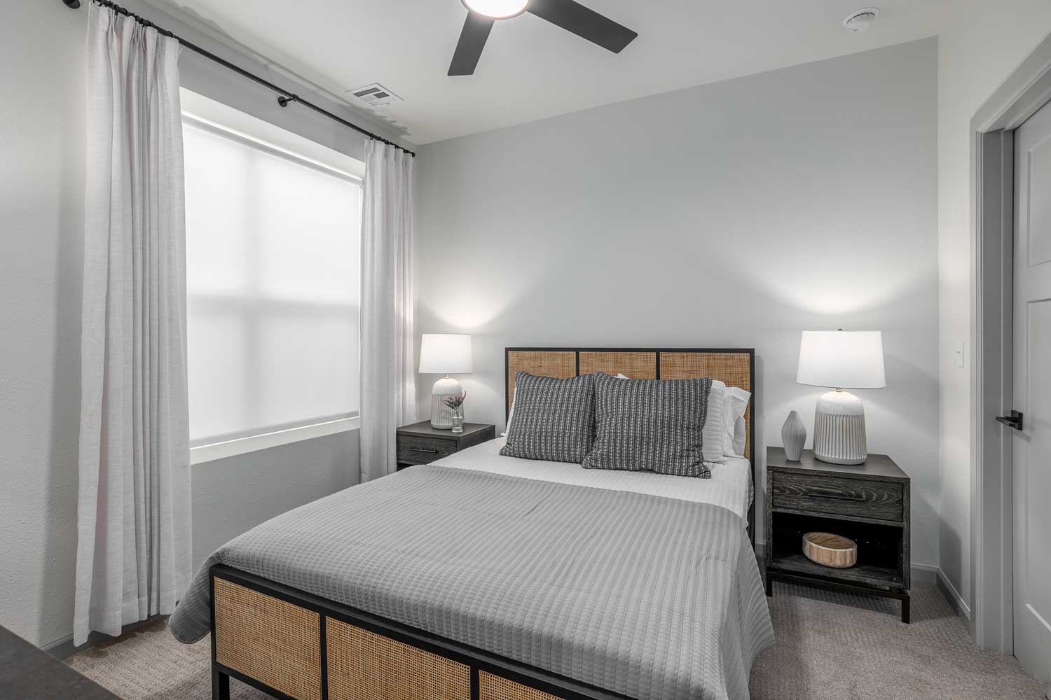 Cozy bedroom with upholstered bed, matching nightstands, soft carpeting, ceiling fan, and window with curtains