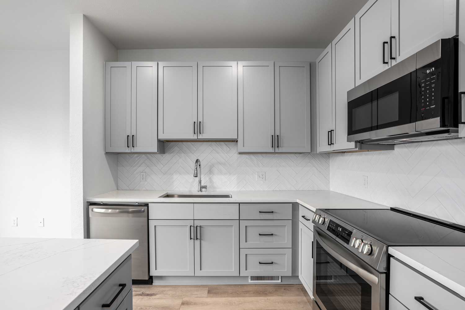 Contemporary kitchen with gray cabinetry, herringbone tile backsplash, quartz counters, and stainless steel appliances