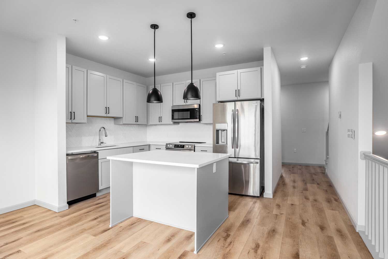 Modern kitchen with center island, pendant lighting, stainless steel appliances, and wood-style flooring below