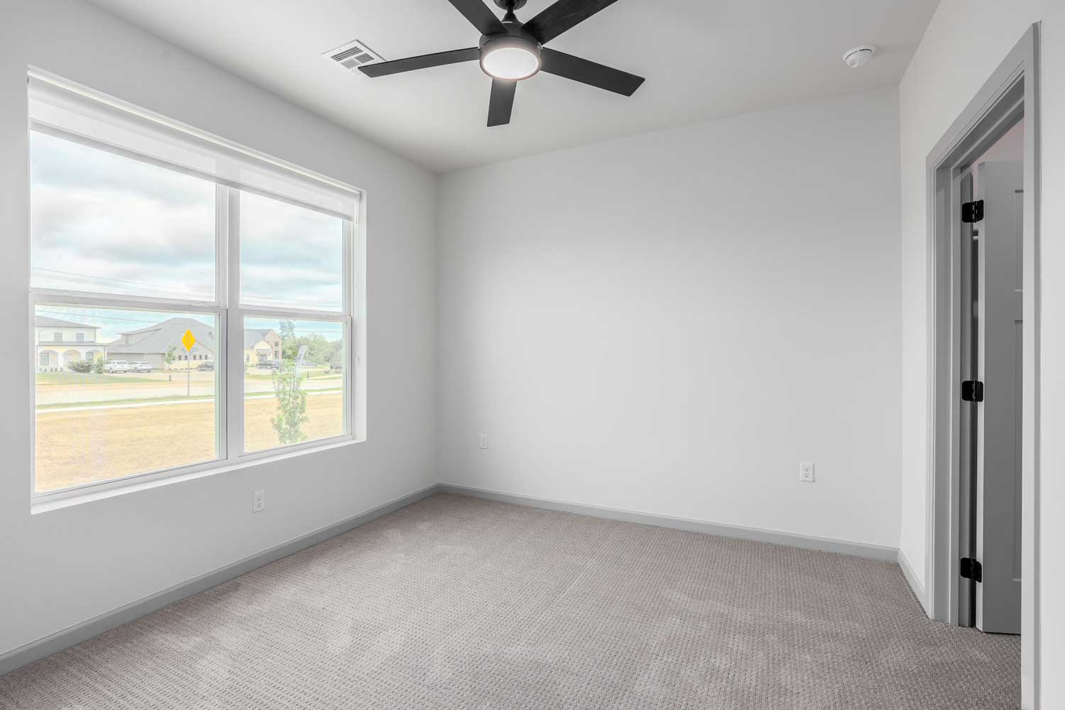 Spacious bedroom with ceiling fan, large window, soft carpet flooring, neutral walls, and neighborhood views outside