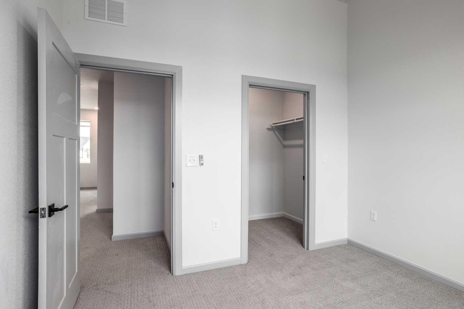 Carpeted bedroom with open doorway, walk-in closet, gray trim accents, neutral walls, and soft natural lighting