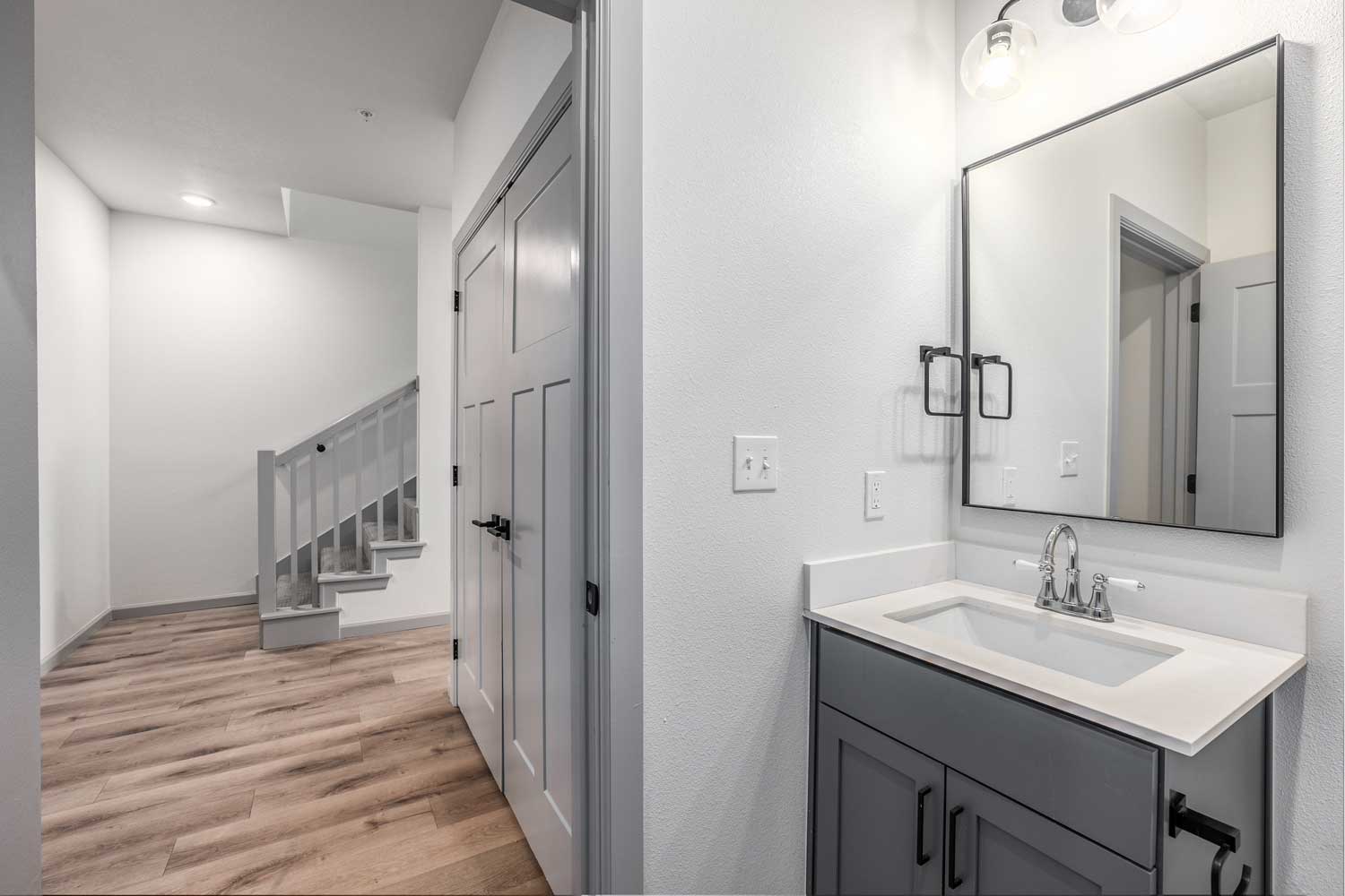 Entry hallway with wood-style flooring, staircase railing, gray vanity cabinet, framed mirror, and recessed lighting