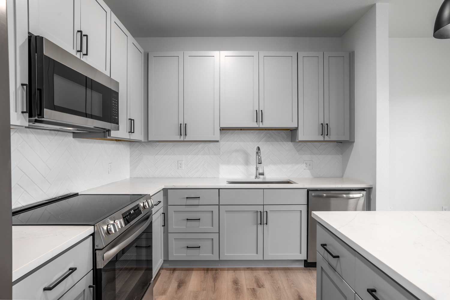 Contemporary kitchen with gray cabinetry, stainless steel appliances, white counters, tile backsplash, and modern fixtures